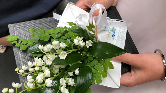 Eine Person hält einen Strauß weißer Blumen und eine Geschenkbox.