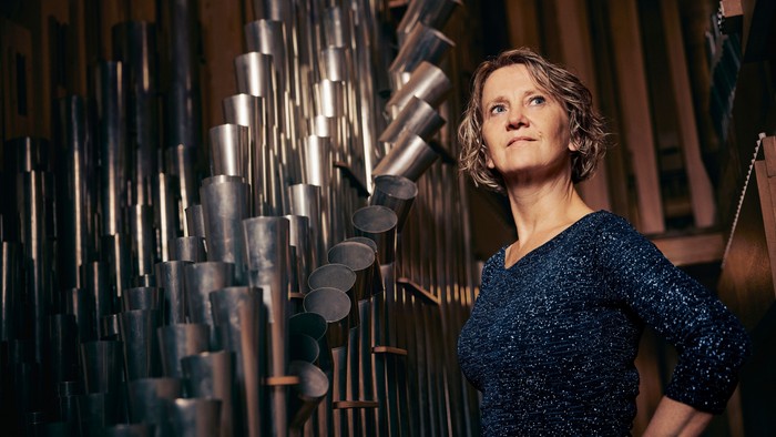 En kvinde står ved siden af et stort, indviklet rørformet musikinstrument, sandsynligvis et rørklokkespil.