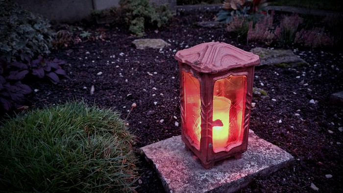 Ein roter Leuchter steht auf einem Stein in einem Garten.