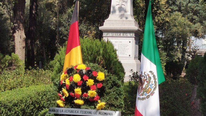 Zwei Flaggen und ein Blumenkranz vor einem Denkmal