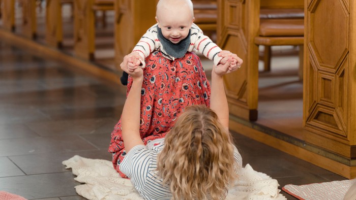 Et barn spiller med en kvinde på gulvmatte i et rum med træmøbler