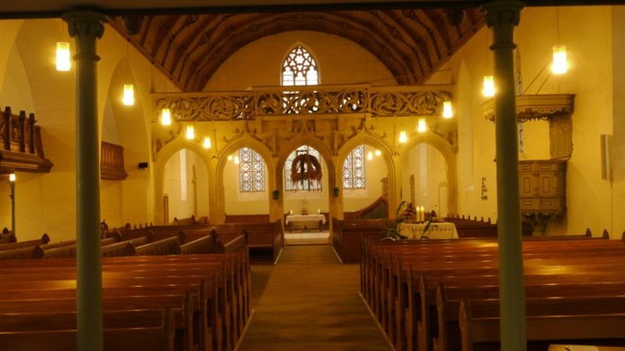 Innenraum einer Kirche mit hölzernen Bänken und hohen Fenstern