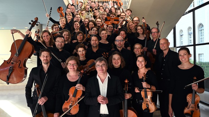 Ein Orchester posiert mit seinen Instrumenten in einem großen Raum