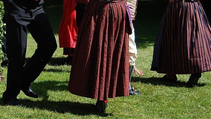 Mehrere Personen in traditioneller Kleidung gehen auf einem grasbewachsenen Bereich.