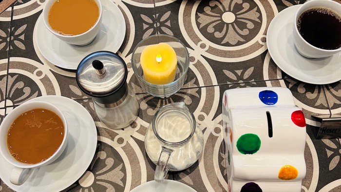 Mehrere Tassen Kaffee und Tee auf einem Tisch mit Mustertischdecke