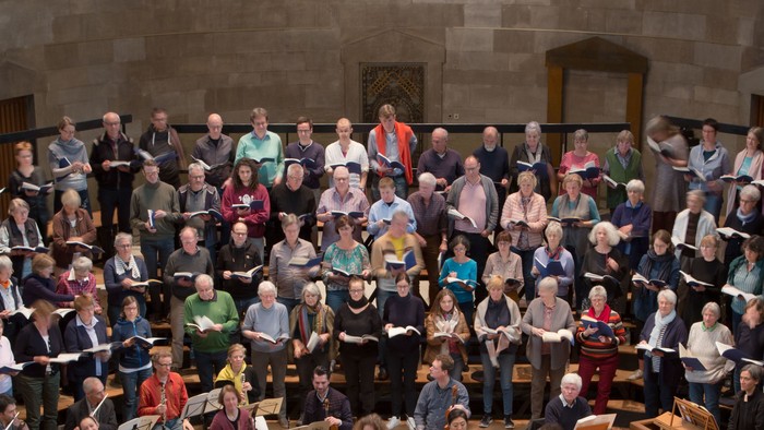 Große Gruppe von Menschen in einem Raum, viele halten Bücher und Notizblöcke