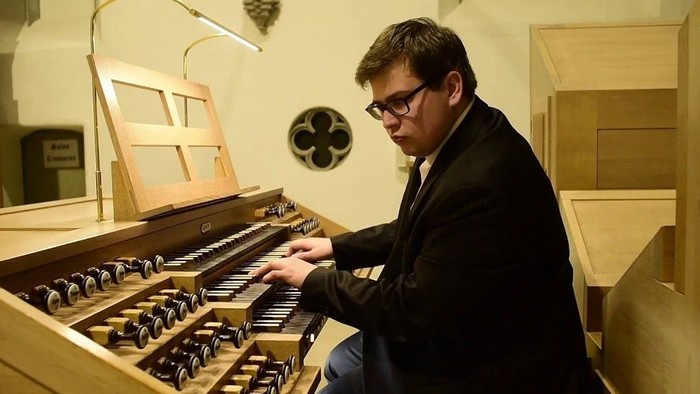 Ein Mann mit Brille spielt eine traditionelle Pfeifenorgel in einer ruhigen Innenraumumgebung.