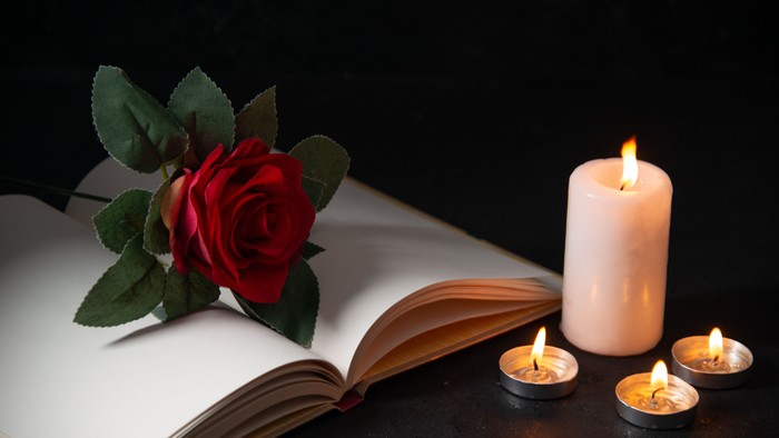 an open Bible with a red rose placed on top of it and 4 lit candles