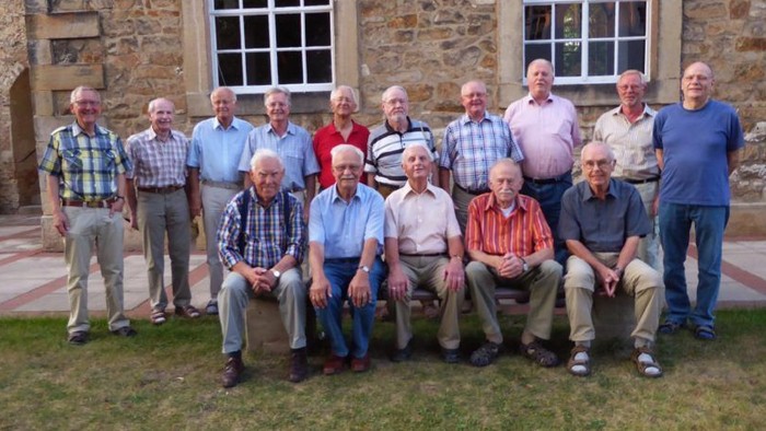 Eine Gruppe älterer Herren posiert vor einem steinernen Gebäude