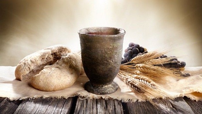A loaf of bread, a cup, and grains displayed on a wooden surface