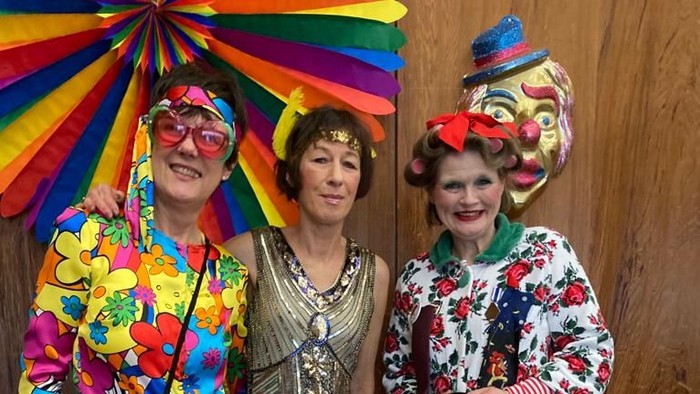 Drei Personen in lebendigen, farbenfrohen und verspielt wirkenden Kostümen, die gemeinsam posieren und eine festliche und ausgelassene Stimmung ausstrahlen.