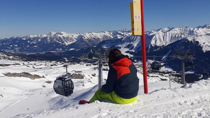 Skifahrer sitzt auf einem Pfosten und schaut auf schneebedeckte Berge