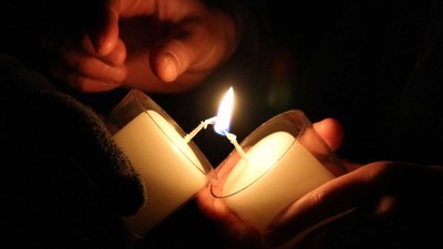 Zwei Hände halten Kerzen im Dunkeln an