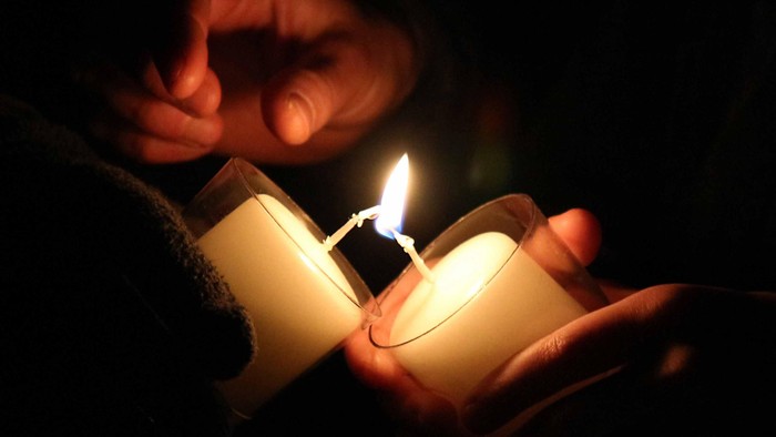 Zwei Hände halten Kerzen im Dunkeln an