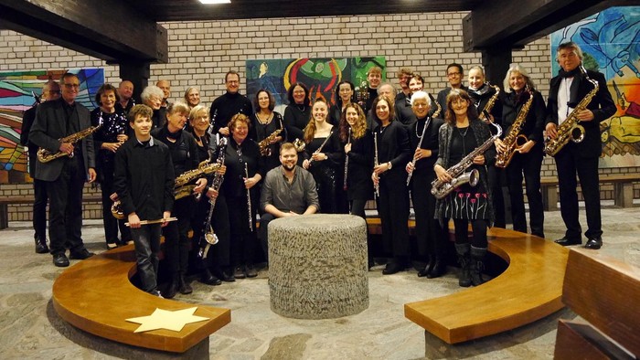 Eine vielfältige Gruppe von Saxophonist:innen posiert gemeinsam in einem farbenfrohen, künstlerischen Innenraum.