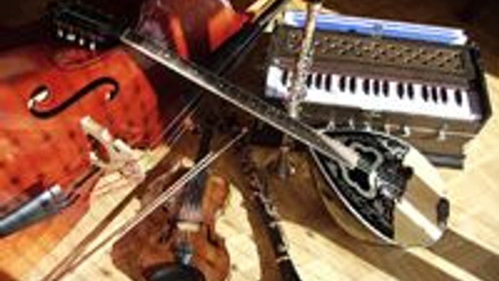 Verschiedene Musikinstrumente, darunter eine Geige und ein Keyboard, liegen auf einem Holzboden.