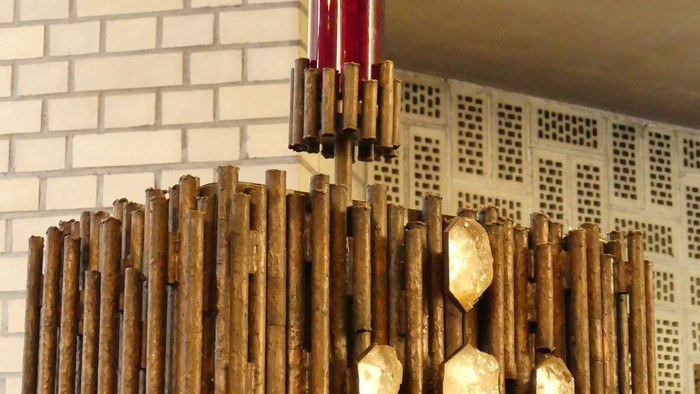 Ein hölzerner Kronleuchter mit goldenen Akzenten vor einer weißen Ziegelwand.