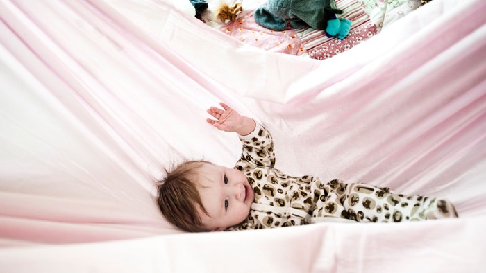 Et spæd barn ligger i en hammock og ser op.