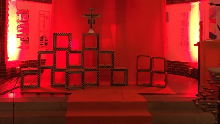 Die Kirche ist in rotes Licht getaucht, der Altar ist mit einem Kreuz geschmückt.