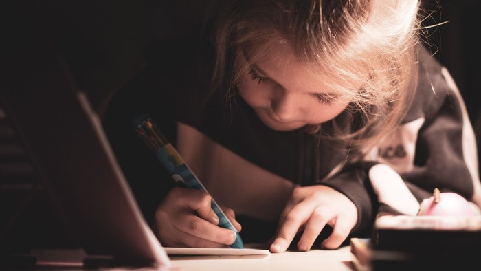 Ein Mädchen schreibt in ein Buch, während sie einen Laptop daneben hat.
