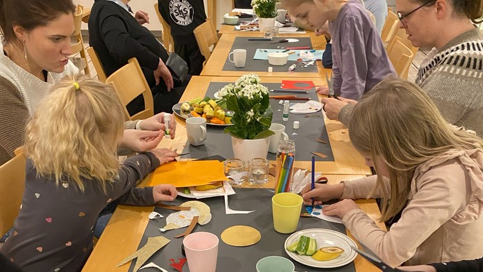 En gruppe af børn og voksne sidder ved et bord og laver håndværk.