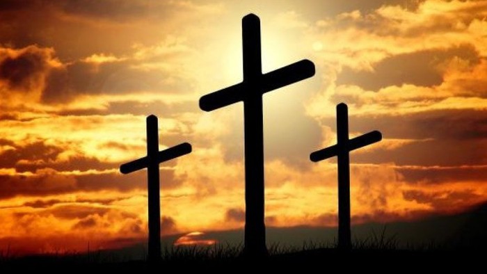 Tre kors stiger op mod en dramatisk solnedgangshimmel.