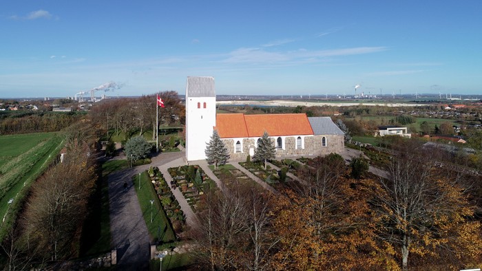 En lille kirke med klokketårn og rødt tag i landlig omgivelse