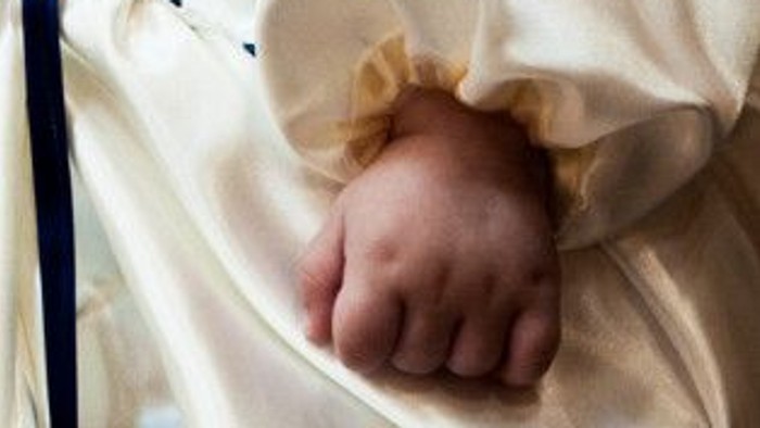 Et spæd barns hånd stikker ud af en hvid pude.