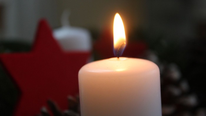 Brennende weiße Kerze, Tannengrün, roter Stern im Hintergrund