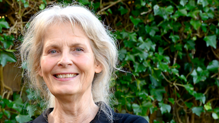 En kvinde med gråt hår smiler varmt udendørs.