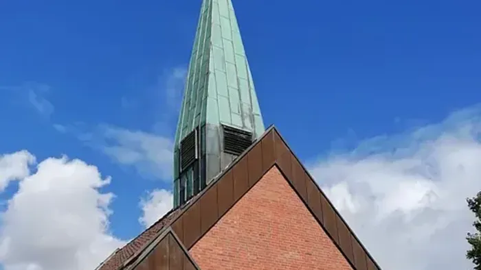 Kirche mit hohem grünem Turmspitz und Kreuz vor blauem Himmel.