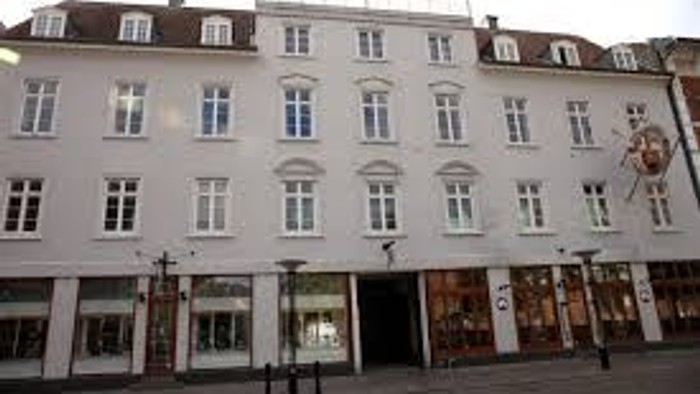 Et stort, hvide bolig- og butikshus med mange vinduer og en central indgang.