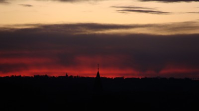 Sonnenuntergang mit dunkler Silhouette eines Kirchturms und Bäumen.