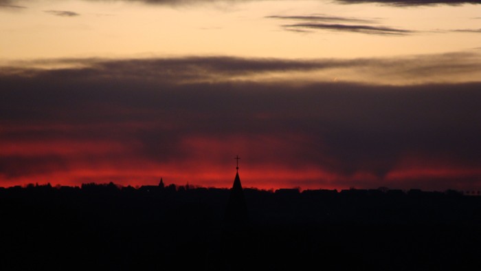 Sonnenuntergang mit dunkler Silhouette eines Kirchturms und Bäumen.