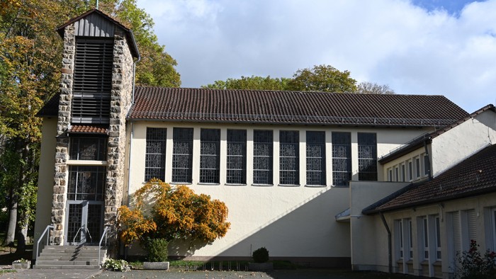 Das Bild zeigt ein modernes Gebäude mit markantem Turm und großen Fenstern, umgeben von Bäumen und einem klaren Himmel.