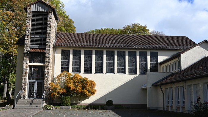 Das Bild zeigt ein modernes Gebäude mit markantem Turm und großen Fenstern, umgeben von Bäumen und einem klaren Himmel.