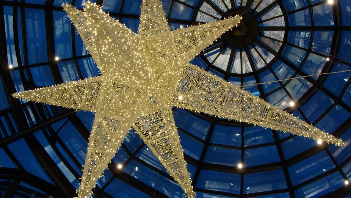 Ein großer, beleuchteter Stern hängt an der Decke eines Glasdaches