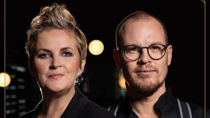 Zwei Personen posieren zusammen, eine Frau mit kurzen blonden Haaren, ein Mann mit Brille und Bart.