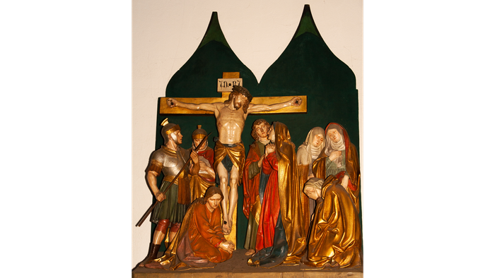 Das Bild zeigt eine religiöse Szene mit Jesus am Kreuz und mehreren Personen in traditioneller Kleidung.