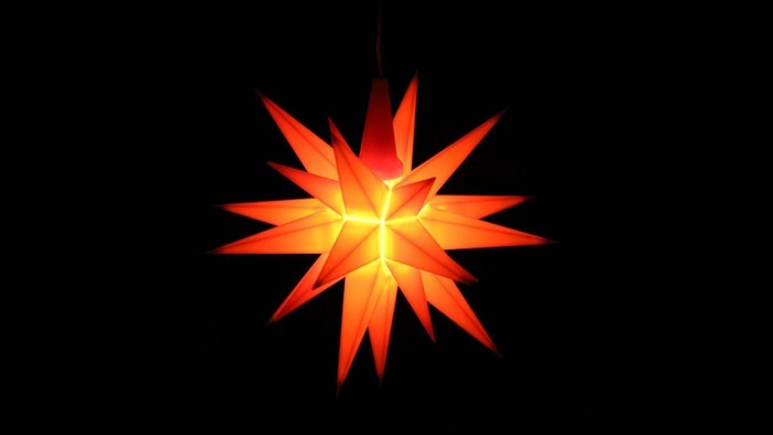 Leuchtender Herrnhuter Stern vor schwarzem Hintergrund