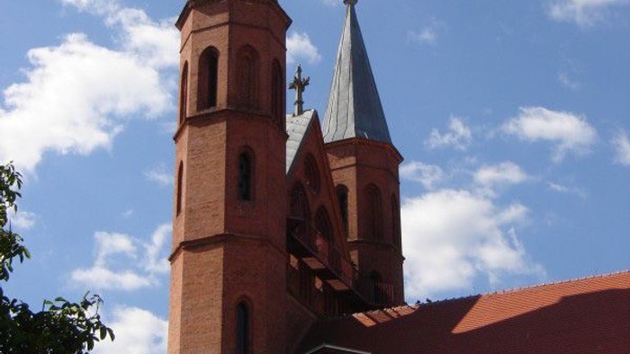 Zwei Kirchtürme mit Kreuz und Wetterfahne vor blauem Himmel