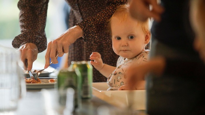 Et barn spiser med en spork og bliver hjalpet af en voksende.