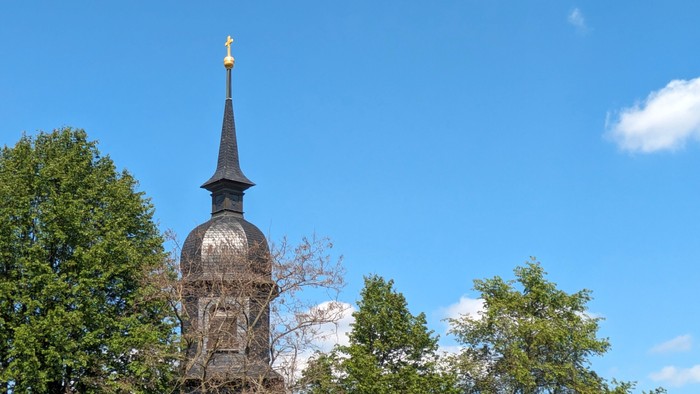 Ein hoher Turm mit spitzer Spitze und goldenem Zierdekor ragt in den klaren blauen Himmel.
