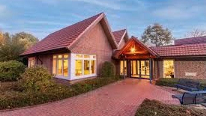 Ein modernes Haus mit großen Fenstern und einer Einfahrt, umgeben von Grün.