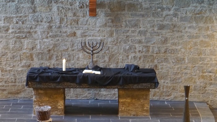 Ein Altar mit Kreuz, Menora und Kerzen in einem Raum mit Steinwänden