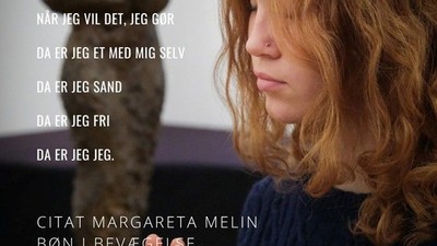 En ung pige med røde lokker og blå trøje ser op og til med hände på brystet.