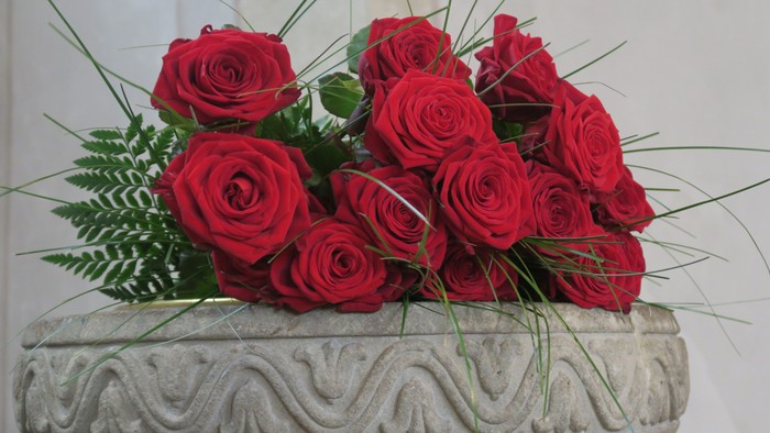 Hier sieht man den oberen Rand des Taufsteins in der Johanneskirche mit Ornamenten. Darauf liegen einige rote Rosen.