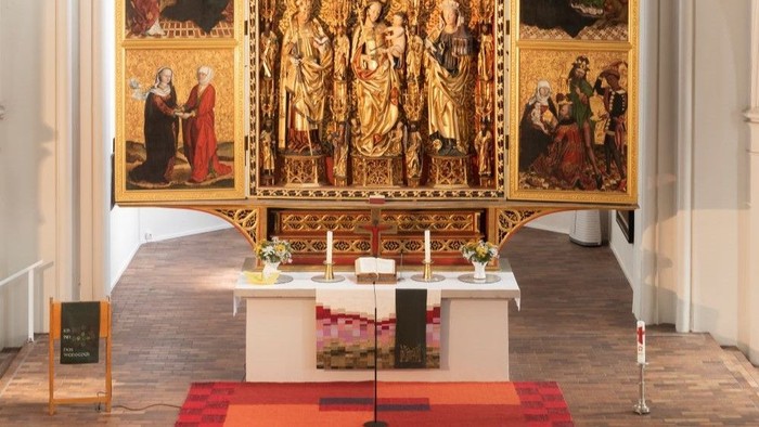 Altar mit Bibel und Kerzen, daneben ein Lesepult, im Hintergrund ein geschnitzter Hochaltar.