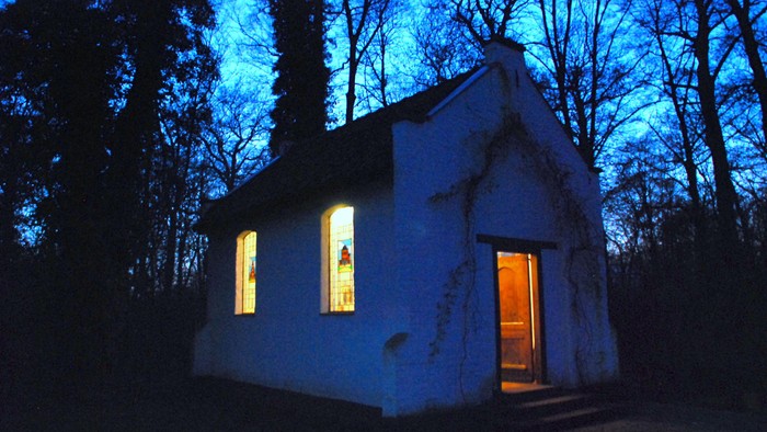 Kleines weißes Haus im Wald bei Nacht, erleuchtete Fenster