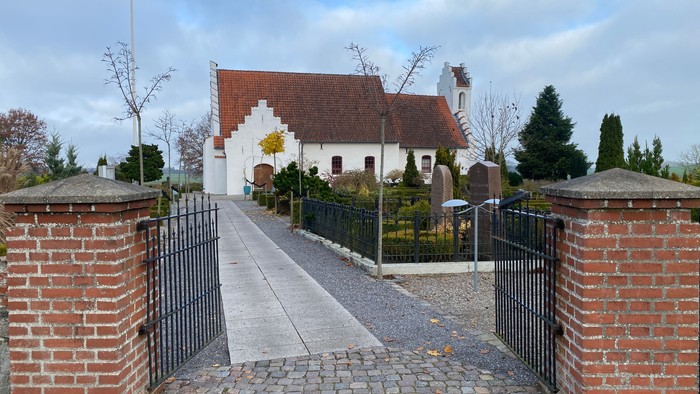 En smuk kirke med røde tag og hvidt udseende, omgivet af en mur og en sti.